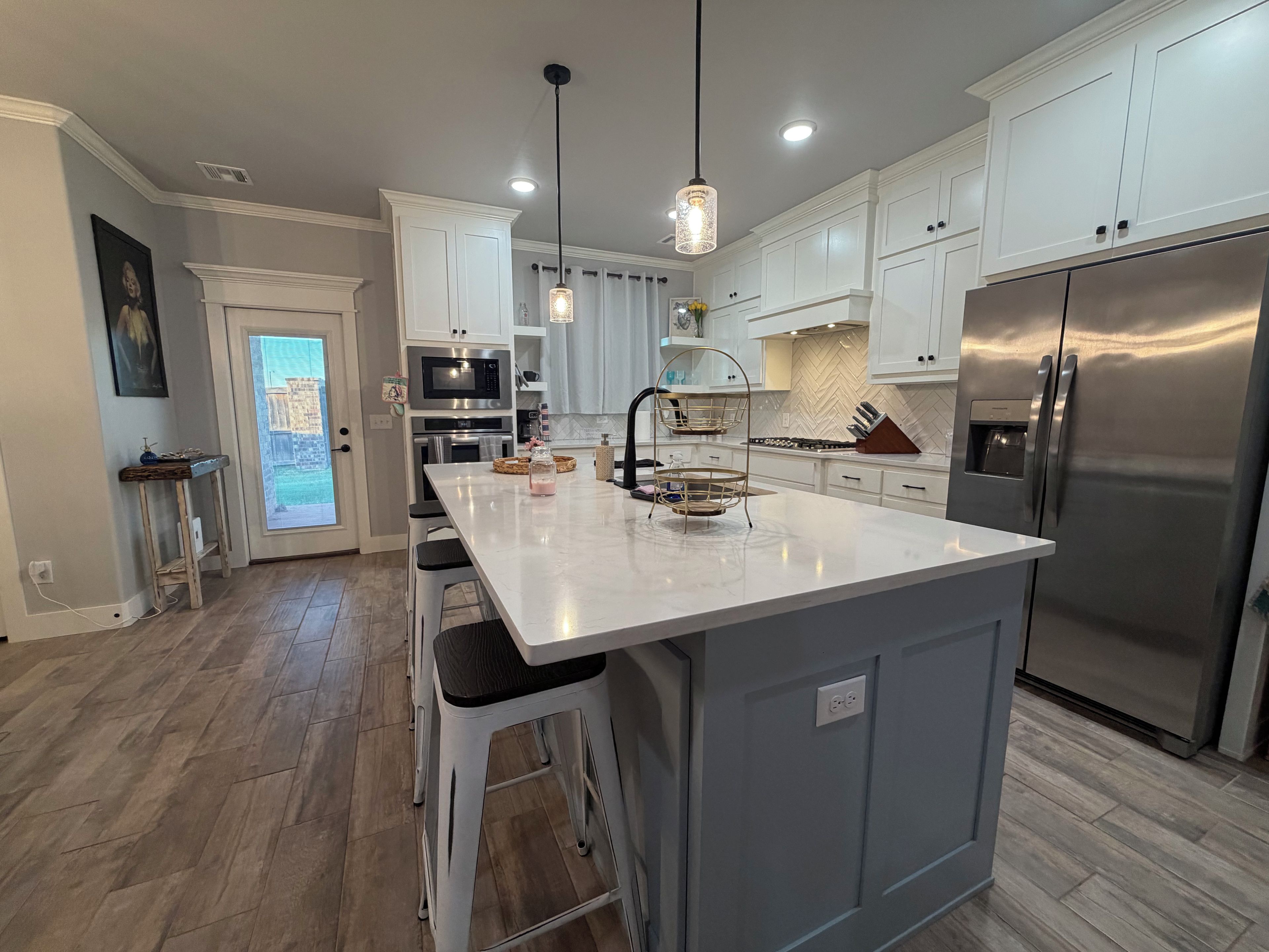 A modern kitchen with a large island, stainless steel appliances, and pendant lighting.