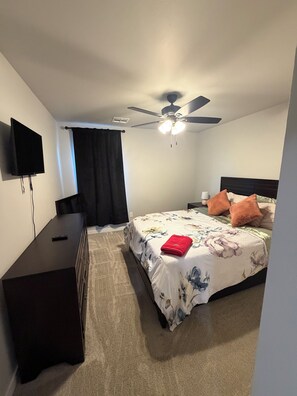 Quarto com cama, ventilador de teto, televisão e cômoda.