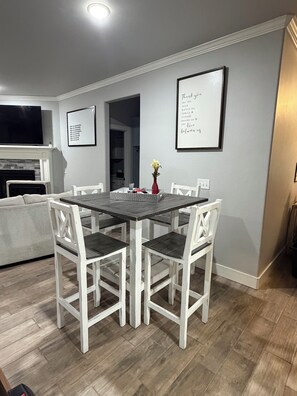 A dining area with a white table and chairs, a fireplace, and a framed message on the wall. - Edmond 4BR Entertainment Retreat, Pool Table, Air Hockey, Ping Pong & Sleeps 10 (Edmond)