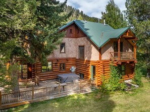 A log cabin with a balcony, a covered patio, and a view of the surrounding forest. - NEW | Private Hot Tub | Hike | Gallatin Canyon, Fire Pit, Sleeps 12 (Gallatin Gateway)