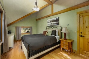 A bedroom with a bed, a bedside table with a lamp, a wooden door, and a window with curtains. - NEW | Private Hot Tub | Hike | Gallatin Canyon, Fire Pit, Sleeps 12 (Gallatin Gateway)