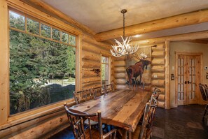 A log cabin interior with a large dining table, wooden chairs, a chandelier, and a mural of a moose. - NEW | Private Hot Tub | Hike | Gallatin Canyon, Fire Pit, Sleeps 12 (Gallatin Gateway)