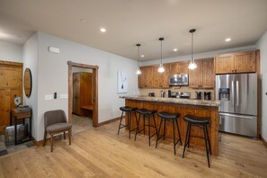 A modern kitchen with wooden cabinets, stainless steel appliances, and a bar area with stools. - New! Private Hot Tub | Town Center | Sleeps 9 (Big Sky)