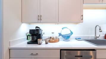 A modern kitchen with a coffee maker, mugs, a basket, and a dishwasher.