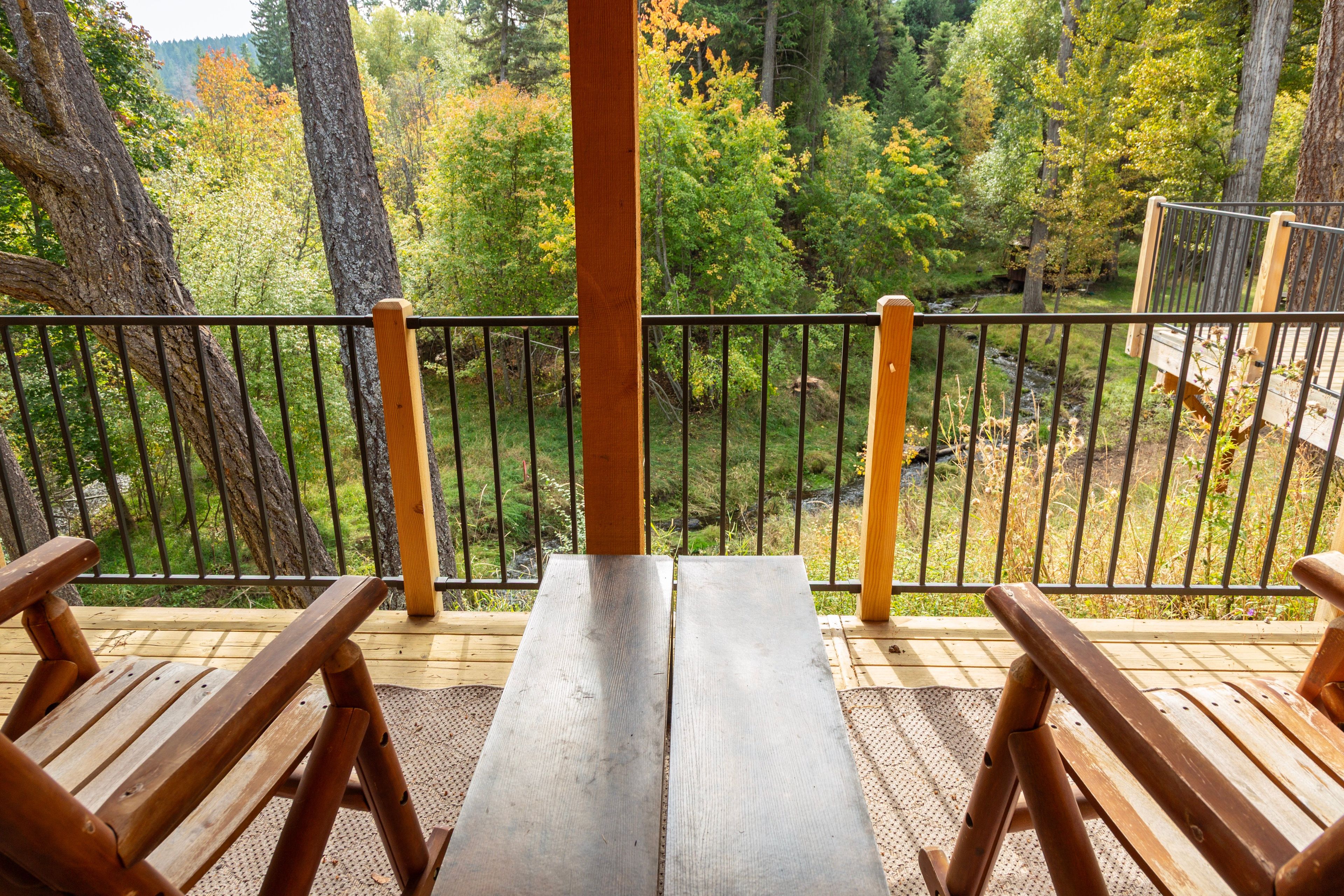 Une terrasse en bois avec un banc et une table, donnant sur une zone boisée.