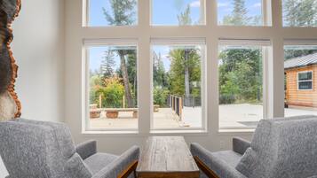 A room with a large window overlooking a deck area with outdoor seating and a view of trees and a building.