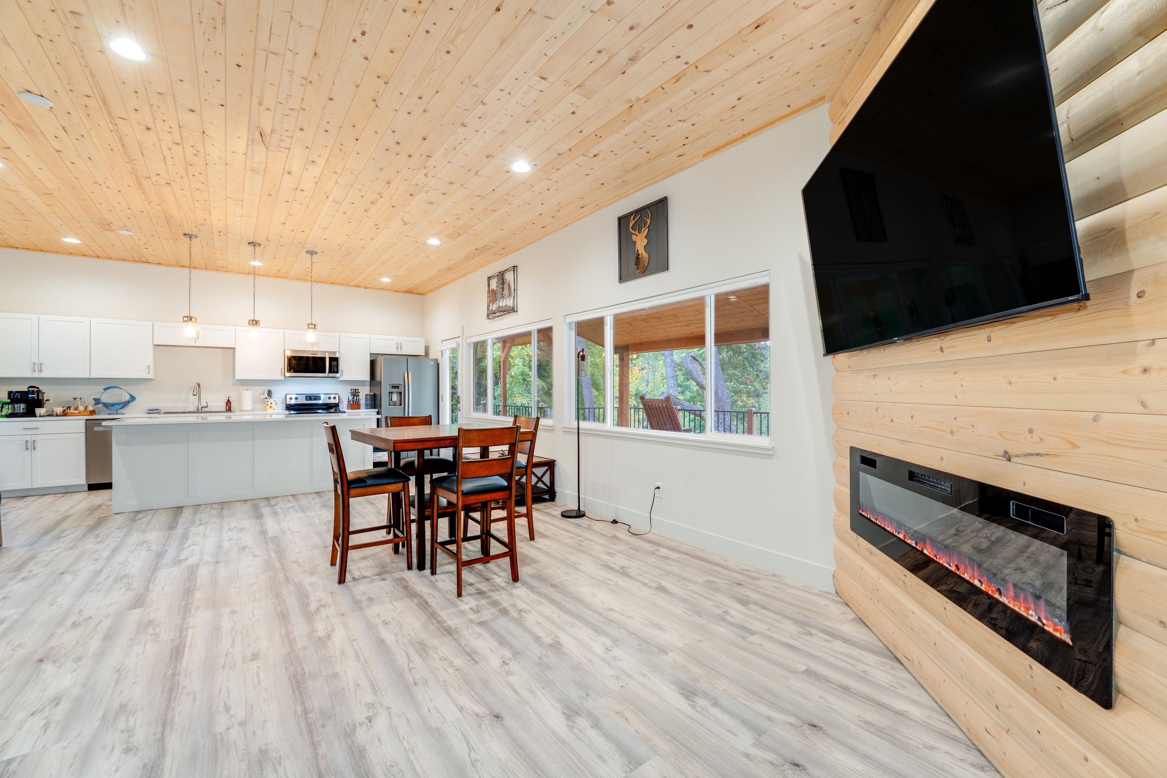 Una cucina moderna con soffitto in legno, mobili bianchi, un'area pranzo con sedie e un camino.