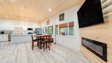 Una cucina moderna con soffitto in legno, mobili bianchi, un'area pranzo con sedie e un camino.