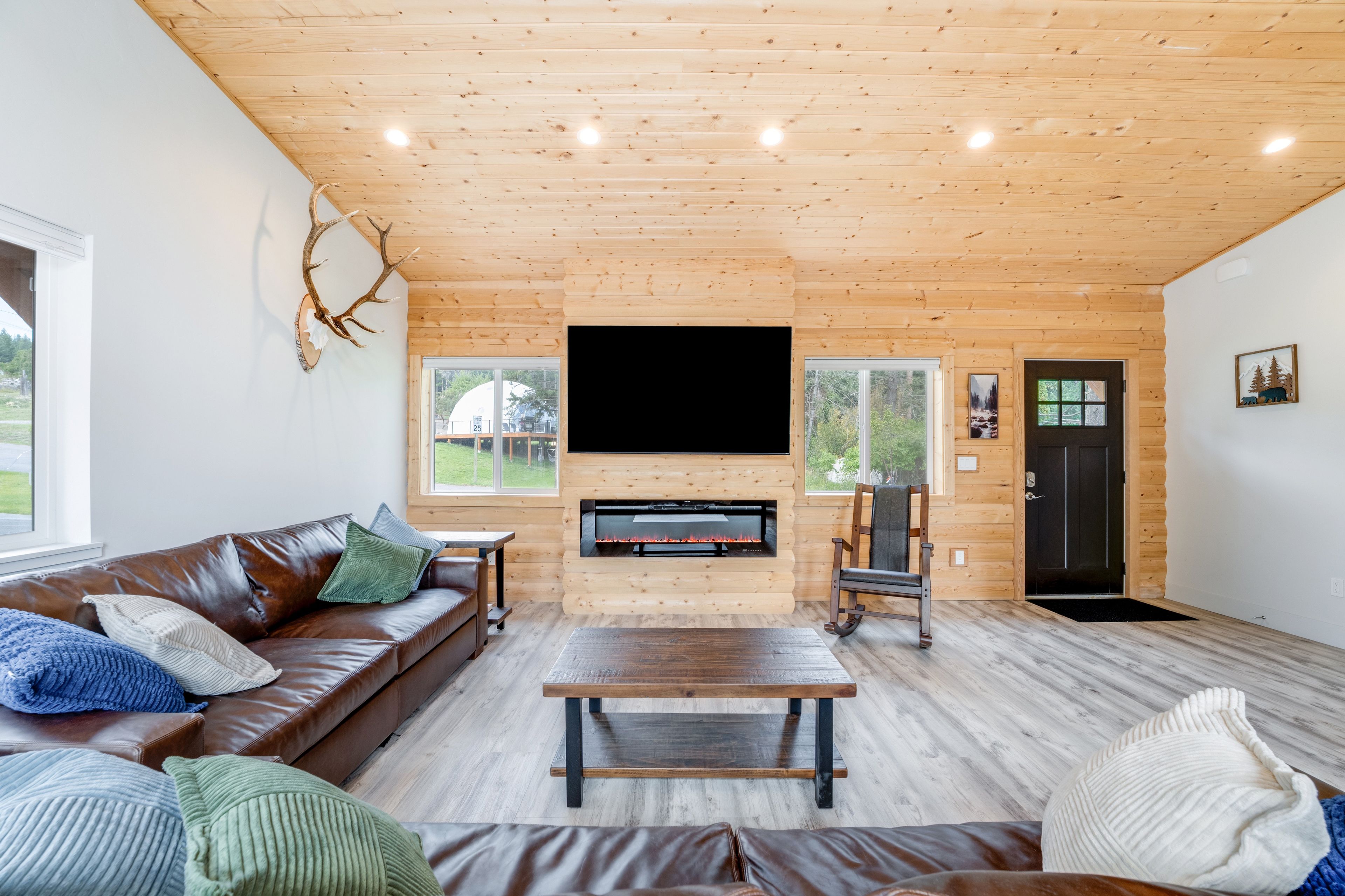 A log cabin interior with a fireplace, leather sofa, and a mounted deer head.