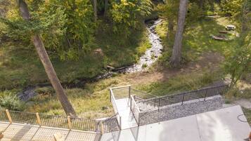 Une terrasse en bois avec une rambarde en métal, donnant sur une zone boisée traversée par un ruisseau.