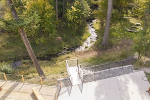 Una terraza de madera con barandilla metálica que da vista a un bosque con un arroyo.