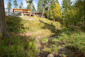 Una cabaña con terraza, rodeada de bosque y un arroyo.