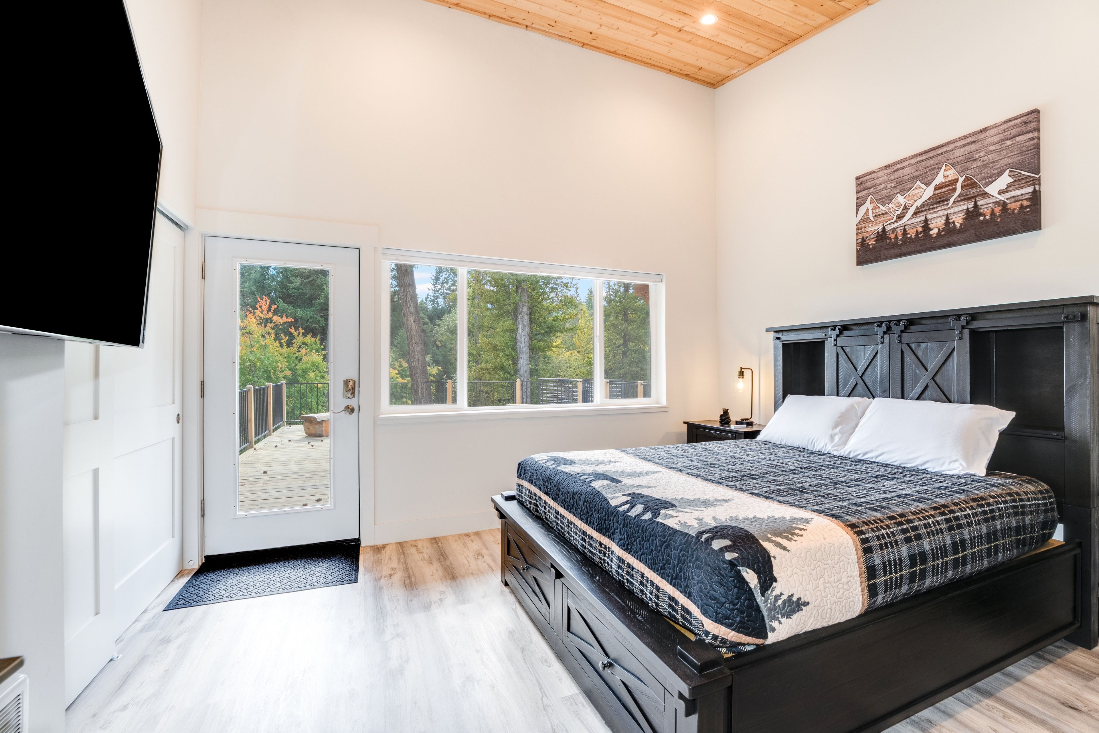 Une chambre avec un grand lit, un plafond en bois, une porte donnant sur un balcon et un tableau accroché au mur.