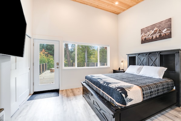 Un dormitorio con una cama grande, techo de madera, una puerta que da a un balcón y un cuadro en la pared.