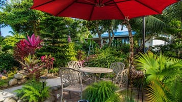 Un patio jardín con un paraguas rojo, sillas de metal y una estatua de jirafa.