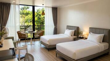 A hotel room with two beds, a dining table, chairs, and a balcony with curtains.