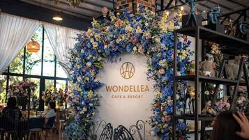 A cafe interior with a floral arch and a logo, tables, chairs, and a brick wall.
