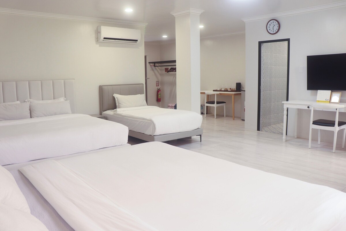 Une chambre d’hôtel avec deux lits, un bureau, une chaise, une télévision et une horloge au mur.