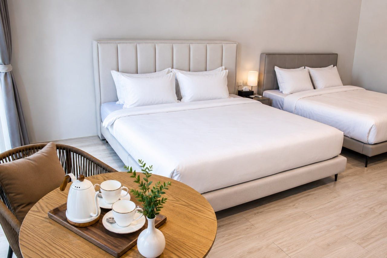 A hotel room with two beds, a round table with a tea set, and a wicker chair.