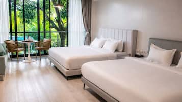 Habitación de hotel con dos camas, una pequeña mesa con sillas y vista a zonas verdes a través de amplios ventanales.