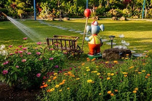 Un jardin agrémenté d’un élément aquatique, d’une charrette en bois et d’une statue représentant un personnage.