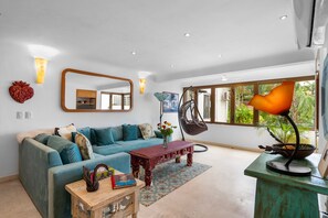 A modern living room with a sofa, a coffee table, a hanging chair, and a large window with a view of greenery. - Casita Espléndida 2 Blocks from the Beach (Puerto Vallarta)