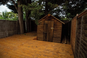 A wooden shed with a door and a small opening, surrounded by a wooden fence and trees. - Central Wembley - Apartment - Sleeps 5 - Parking (Wembley)