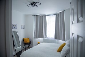 Une chambre d’hôtel avec un lit, une chaise, un radiateur et une fenêtre avec des rideaux.