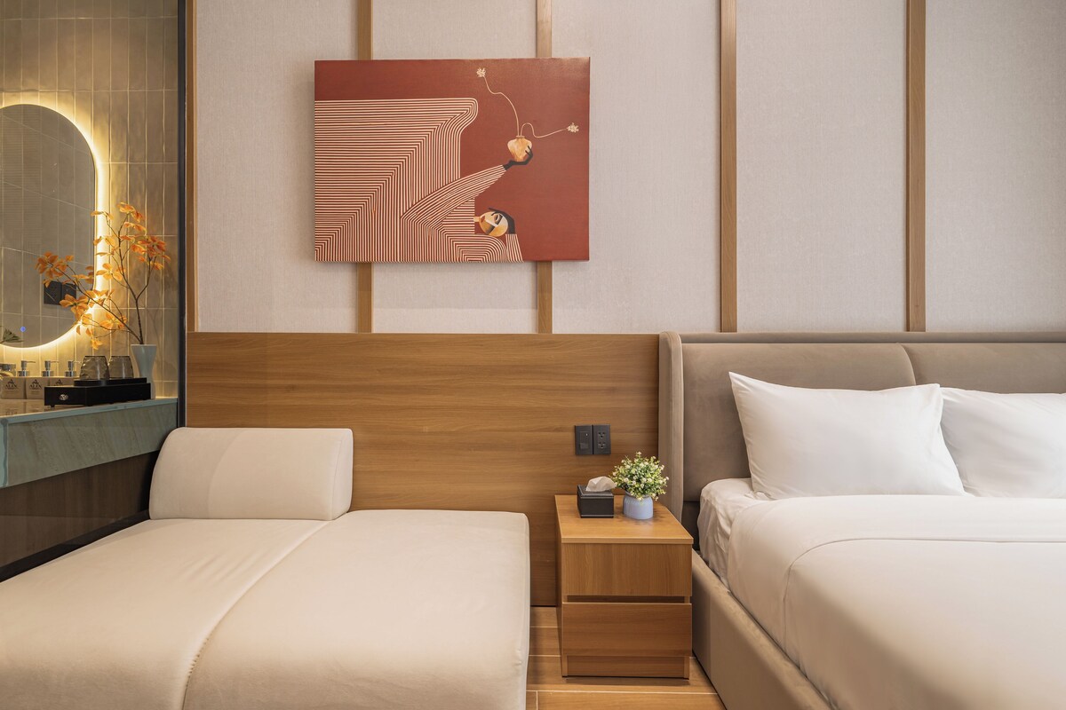 A hotel room with a bed, bedside tables, a nightstand, a mirror, and a wall-mounted artwork.