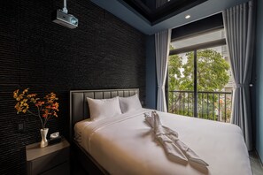 Ein modernes Hotelzimmer mit einem großen Bett, einem Projektor, einem Nachttisch mit Blumen und Blick auf Grünfläche.