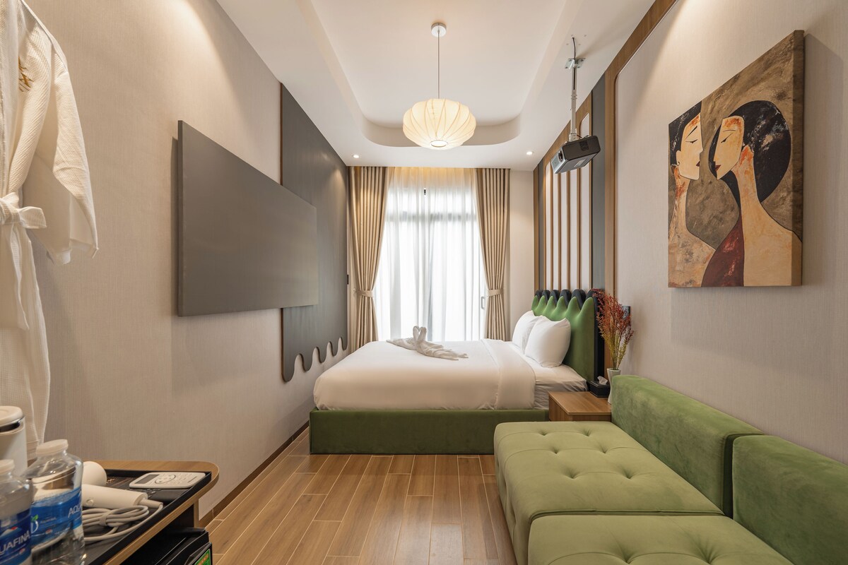 A hotel room with a bed, a green sofa, a TV, and a painting on the wall.