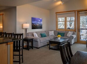 A living room with a sofa, chairs, a coffee table, a lamp, and a window with a view of snow-covered trees. - Grand Timber Lodge 1bd, Hot Tubs, Pools & Saunas (Breckenridge)