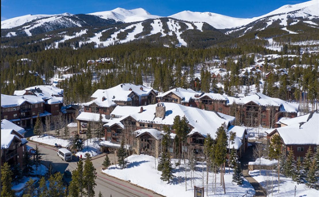 A snow-covered mountain town with lodge-style buildings, a clear sky, and a road leading through the area.