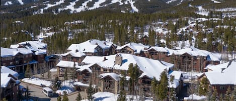 A snow-covered mountain town with lodge-style buildings, a clear sky, and a road leading through the area.