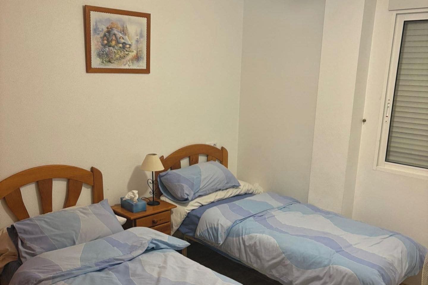 Un dormitorio con dos camas individuales, una mesita de noche con lámpara y un cuadro en la pared.