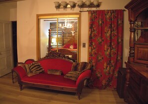 A room with a red sofa, a wooden cabinet, and a mirror reflecting a chandelier. - Nestled in a pine forest close to 4 parks including Algonquin.  Rustic log house (South River)