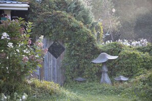 A garden with a wooden fence, a stone birdbath, and lush greenery. - Nestled in a pine forest close to 4 parks including Algonquin.  Rustic log house (South River)