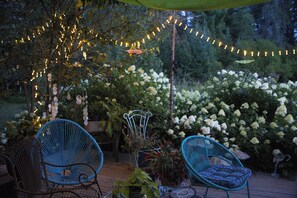 A patio with two blue chairs, a table, and a string of lights. - Nestled in a pine forest close to 4 parks including Algonquin.  Rustic log house (South River)