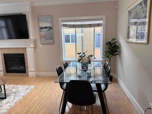 A dining area with a glass table, black chairs, a vase with flowers, and a fireplace. - V-2Spaces one area-near PNE (Vancouver)