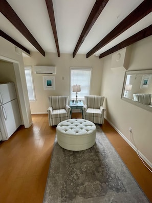 A room with a round ottoman, two striped armchairs, a small table with a lamp, and a refrigerator. - Romantic Carriage House Near Forsyth Park, Parking (Savannah)