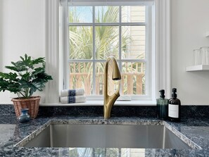Eine Küche mit einem goldenen Wasserhahn, einem Blumentopf und einem Fenster mit Blick auf Palmen.