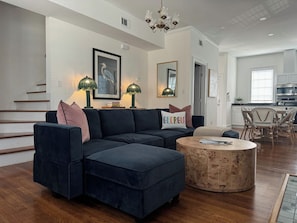 A modern living room with a sectional sofa, ottoman, and a round coffee table. - Historic Downtown Estate | Duplex & Carriage House (Savannah)