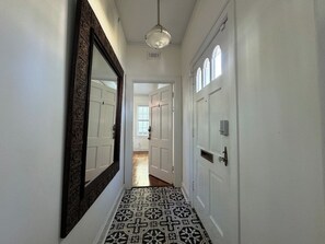 A hallway with patterned flooring, a large mirror, and white doors. - Historic Downtown Estate | Duplex & Carriage House (Savannah)