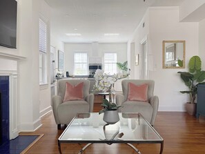 A spacious living room with a glass coffee table, two armchairs, and a potted plant. - Historic Downtown Estate | Duplex & Carriage House (Savannah)