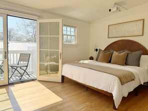 Ein Schlafzimmer mit einem Bett, einer Schiebeglastür, die zu einem Balkon führt, und einem an der Decke befestigten Projektor.