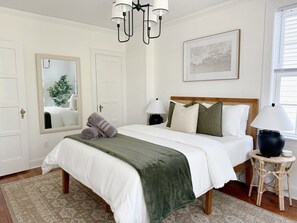 A bedroom with a bed, two bedside tables, a chandelier, a mirror, and a window. - Historic Downtown Estate | Duplex & Carriage House (Savannah)
