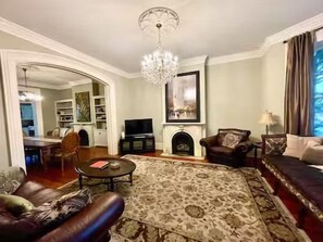 A living room with a fireplace, a chandelier, and a large rug. - Grand 1882 Victorian with 5BR, Steps to Forsyth Park (Savannah)