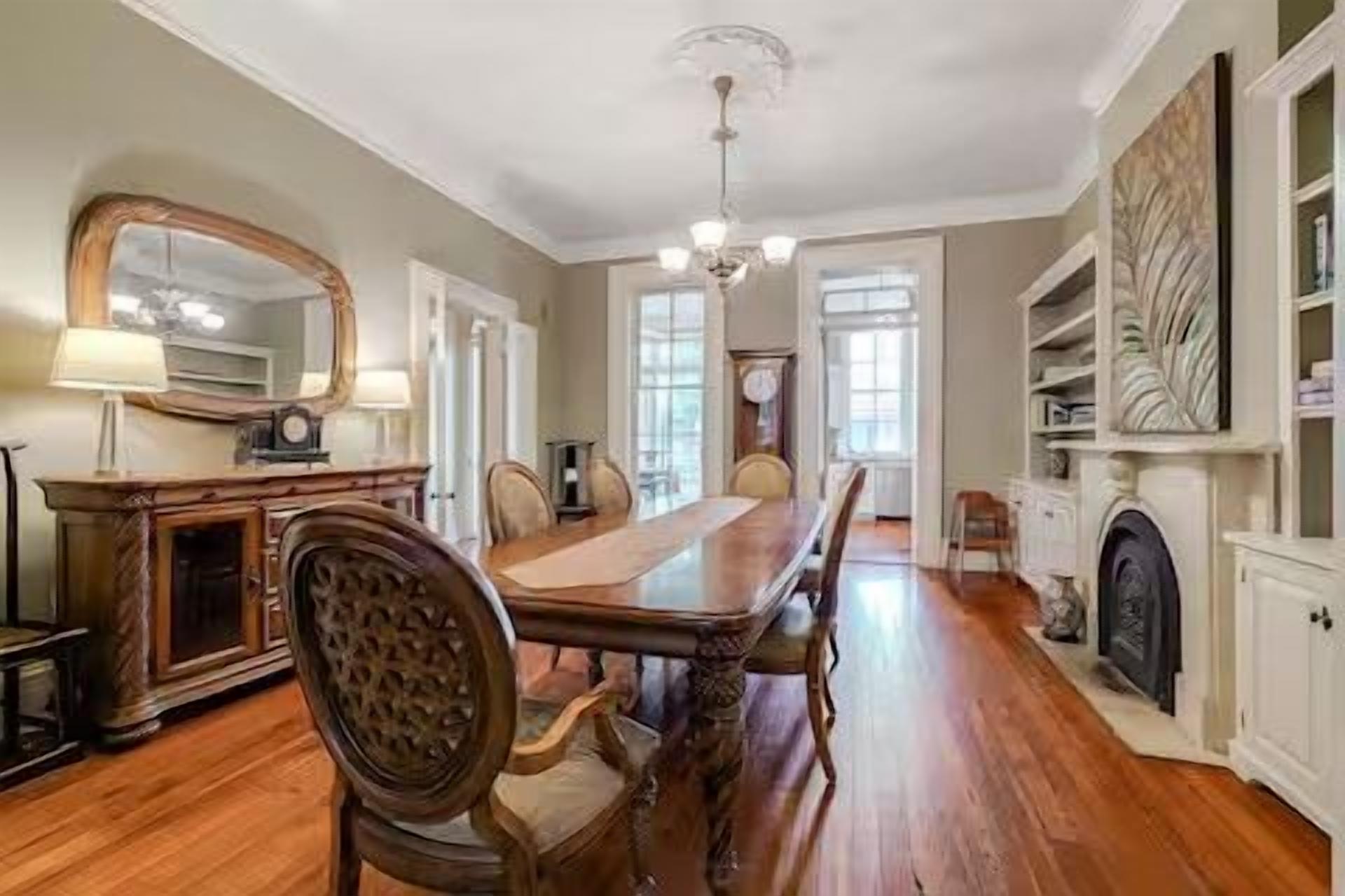 A dining room with a long wooden table, chairs, a chandelier, and a fireplace.