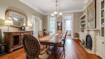 A dining room with a long wooden table, chairs, a chandelier, and a fireplace.