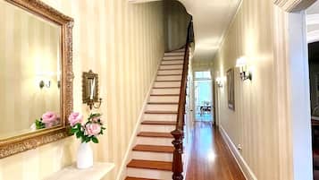 A hallway with a wooden staircase, a chandelier, a mirror, and a vase with flowers.